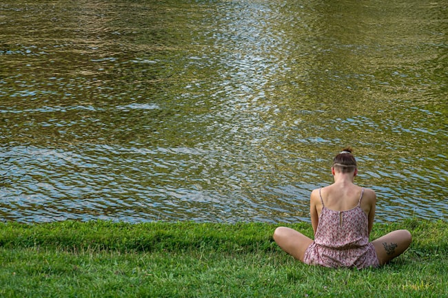 Frau sitzt im Schneidersitz in der Wiese am Wasser