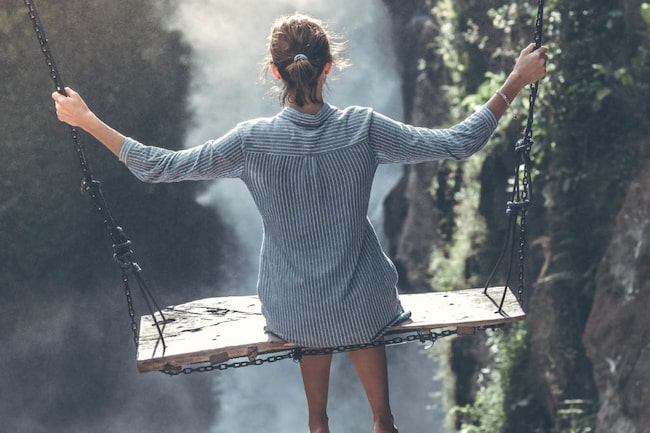 Frau schaukelt über einem Abgrund vor einem Wasserfall