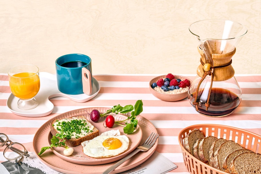 Frühstück, Frühstückstisch, Kaffeekanne, Kaffeetasse, Orangensaft, Butterbrot mit Schnittlauch, Spiegelei, Radieschen, Porridge mit Himberren und Heidelbeeren, Schwarzbrot, Teller, Gabel, Brot, Brotkorb, Zeitschrift, Brille, Ernährung