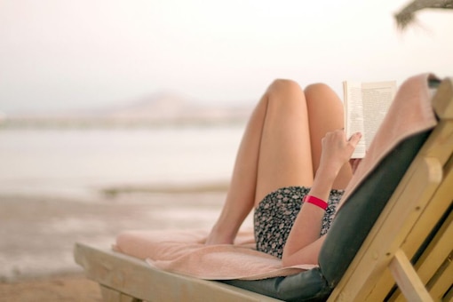 Frau auf Sonnenliege am Meer, liest ein Buch