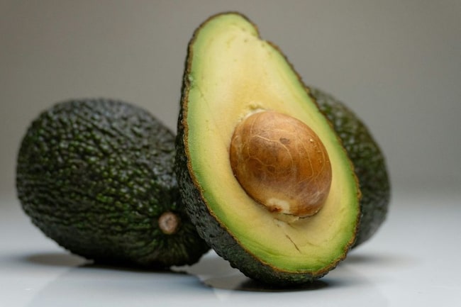 Aufgeschnittene Avocado, im Hintergrund 2 ganze Avocados