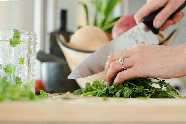 Frauenhand schneidet Gemüse und Kräuter mit Messer