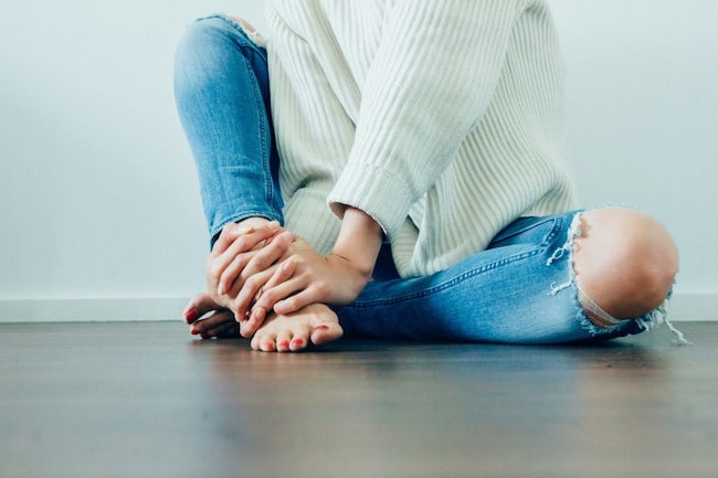 Frau in Jeans am Boden sitzend, Gesicht ist nicht zu sehen.