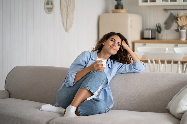 Frau sitzt am Sofa mit Tasse Tee und entspannt