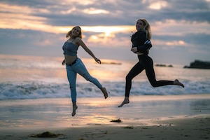 Zwei junge Frauen haben Freude am Laufen, Läuferinnen springen in die Luft, Strand, Sonnenuntergang