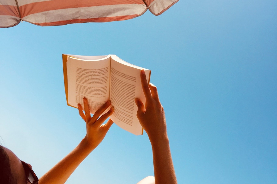 Frau liest Buch unter Sonnenschirm und bei blauem Himmel