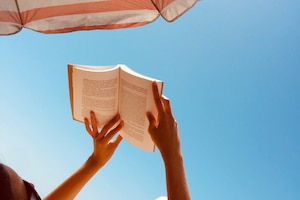 Frau liest Buch unter Sonnenschirm und bei blauem Himmel