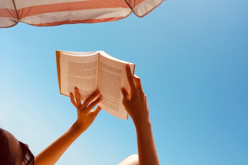 Frau liest Buch unter Sonnenschirm und bei blauem Himmel