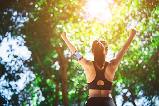 Frau streckt die Arme in die Höhe und genießt die Sonne, Läuferin, Joggerin, Sport, Sportkleidung