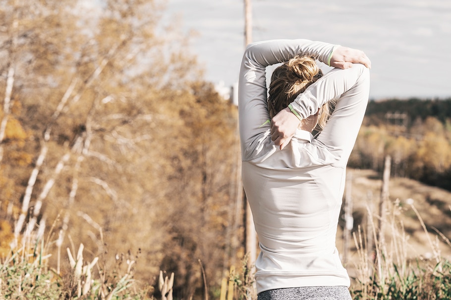 Eine Frau dehnt sich die Arme, Sportlerin in der Natur, Wald, Bäume, Sonnenschein